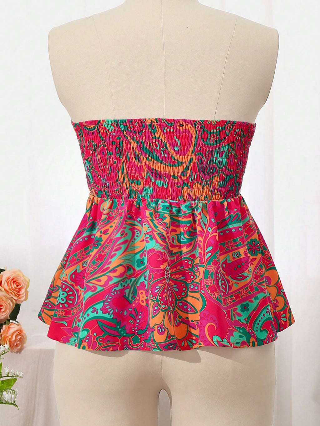 A strapless peplum top with a vibrant multicolor paisley pattern, displayed on a beige mannequin torso.