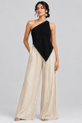 A close-up of a model wearing a black one-shoulder pleated top and a pleated champagne-colored skirt, with silver leaf-shaped earrings.