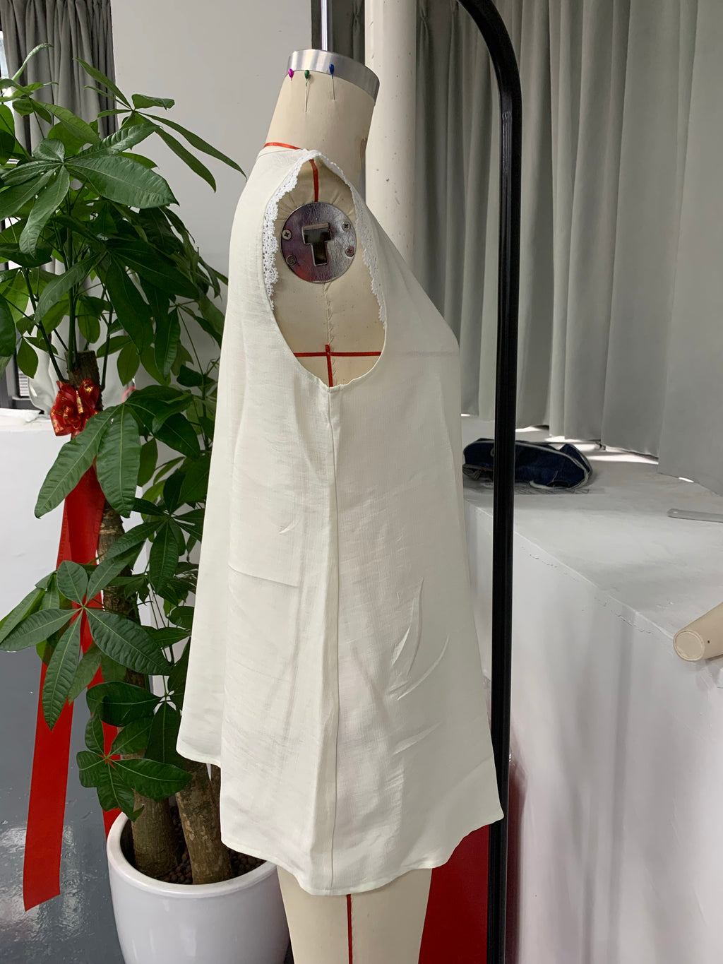 An off-white sleeveless linen top with a raw, unfinished neckline and side pockets, displayed on a dress form mannequin in an indoor studio setting.