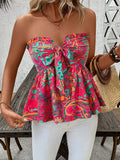 A woman wearing a strapless peplum top with a vibrant multicolor paisley pattern in pink, teal, orange, and green, paired with white pants.