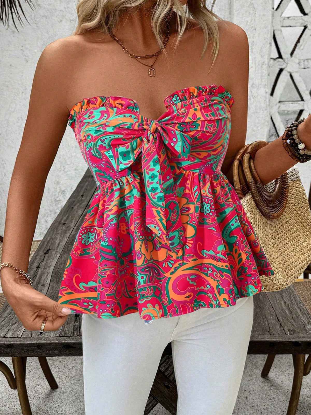 A woman wearing a strapless peplum top with a vibrant multicolor paisley pattern in pink, teal, orange, and green, paired with white pants.