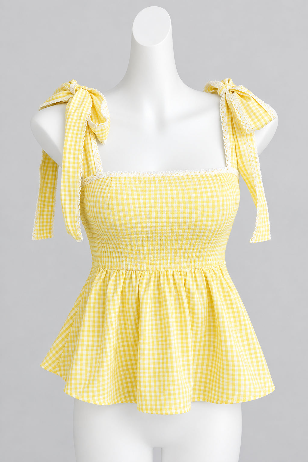 A yellow and white gingham tie-shoulder top displayed on a white mannequin torso against a light gray wall.